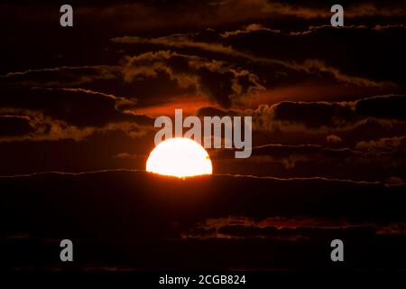 Gros plan du soleil couchant parmi les nuages. Il s'agit d'une image à faible luminosité avec le soleil au milieu et des silhouettes de nuages qui l'entourent. Un paysage Banque D'Images