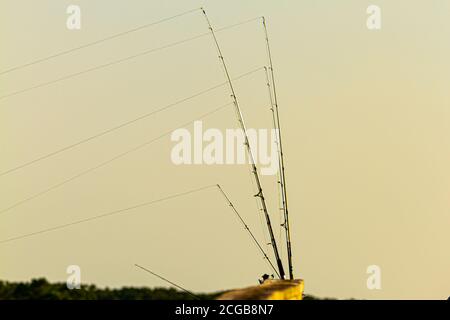 Plusieurs cannes à pêche sont placées sur les rampes en bois d'un pont au coucher du soleil. Ils sont tous mis en place et les pêcheurs (non vus) attendent de vibrer Banque D'Images
