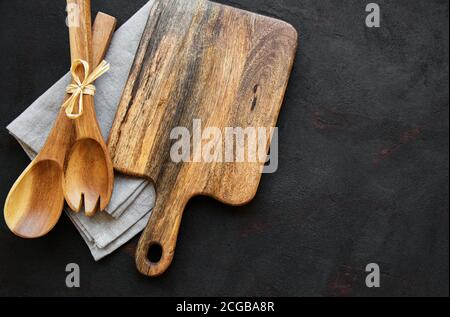 Vieux ustensiles de cuisine vintage. Cuillères en bois, planche à découper, serviette sur fond noir. Vue de dessus Banque D'Images