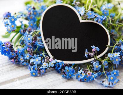 Fleurs oubliées-me-pas et tableau noir en forme de coeur sur fond blanc en bois Banque D'Images