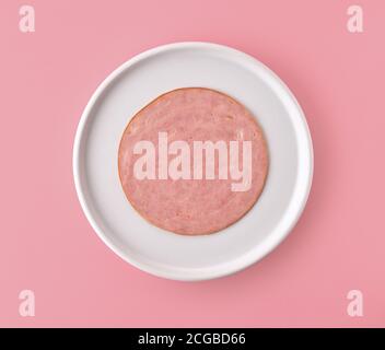 tranche de saucisse de jambon sur plaque blanche isolée sur fond rose, vue du dessus Banque D'Images