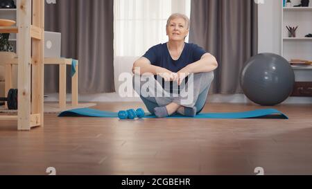 Portrait d'une femme âgée assise sur un tapis de yoga. Active sain style de vie sportif Old personne entraînement bien-être à la maison et l'exercice intérieur Banque D'Images