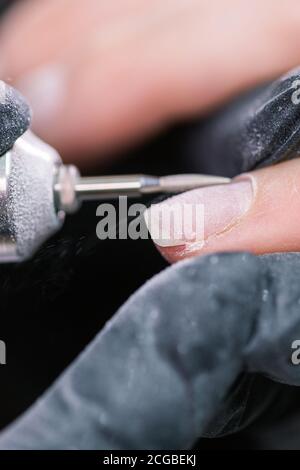 Traiter les gros travaux de manucure. Préparation à la manucure de la quincaillerie. Esthéticienne en gants de caoutchouc coupe la cuticule et traite les ongles. Banque D'Images