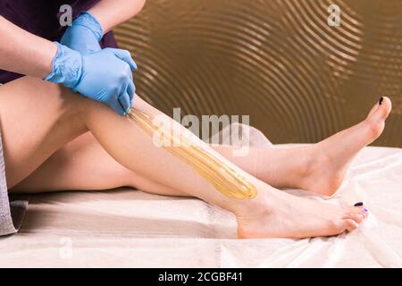 Femme ayant la procédure d'enlèvement de cheveux sur la jambe avec pâte de sugaring en salon, gros plan. Concept de cosmétologie. Banque D'Images