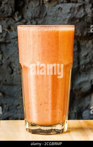 Smoothie aux agrumes d'orange dans un grand verre contre un mur en pierre sombre Banque D'Images