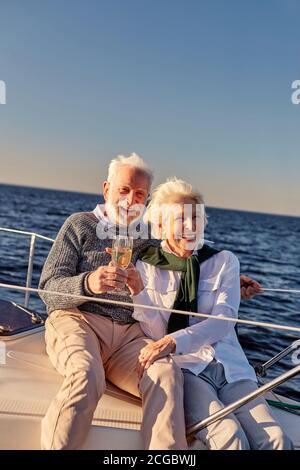 Santé. Un couple familial heureux et expérimenté boit du vin ou du champagne et sourit tout en célébrant son anniversaire de mariage sur un voilier ou une terrasse de yacht flottant Banque D'Images