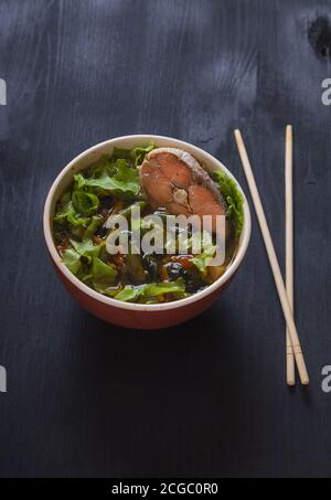 Soupe japonaise au saumon rose, haricots verts et légumes verts, bâtonnets de bambou sur fond noir. Verticale Banque D'Images