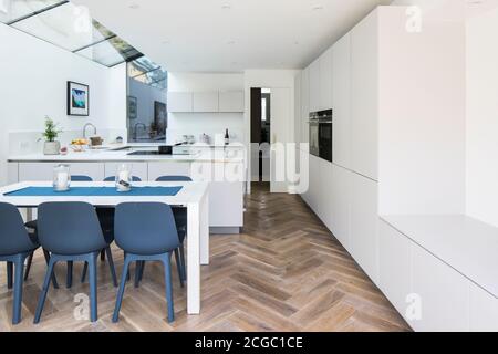 Cuisine moderne avec parquet, cuisine blanche et table à manger avec chaises bleues. Banque D'Images