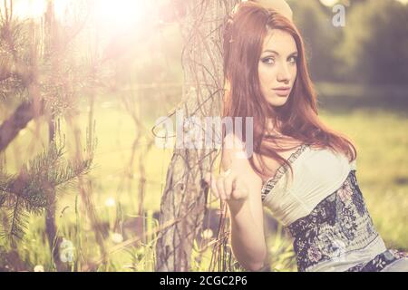 jeune femme à tête rouge portrait en robe vintage près de la vieille terre agricole clôture au coucher du soleil de printemps Banque D'Images