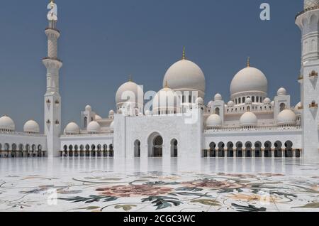 Une photo d'une journée de la Grande Mosquée Sheikh Zayed, dans la cour intérieure centrale d'Abu Dhabi, où deux ouvriers ont poli le sol en marbre. Les caractéristiques architecturales comprennent des dômes, le dôme principal, des arches centrales, des colonnes et le sol en marbre fleuri. Mosquée terminée 2007. Banque D'Images