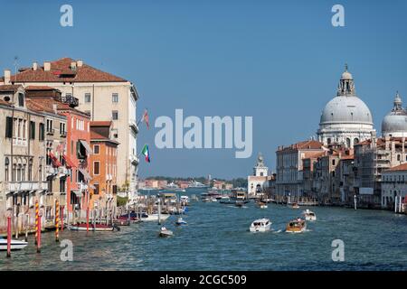 Le Grand Canal de Venise avec une basilique et d'autres bâtiments vernaculaires locaux qui entourent le front d'eau. Une gondole et les habitants de la région dans leurs bateaux sur le canal. Banque D'Images