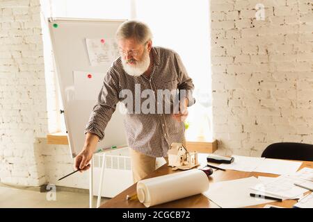 Un architecte-ingénieur de sexe masculin présente un projet de future maison pour la jeune famille. Homme travaillant au bureau avec des documents, un plan. Première maison, industriel, concept de bâtiment. Déplacement vers un nouveau lieu de vie. Banque D'Images