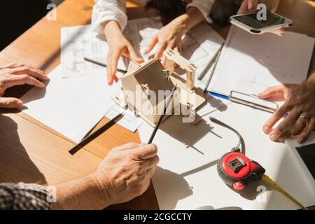 Gros plan des mains de l'architecte-ingénieur et du jeune couple lors de la présentation de la future maison. Table de vue de dessus avec documents, photocalque. Première maison, industriel, concept de bâtiment. Déplacement vers un nouveau lieu de vie. Banque D'Images