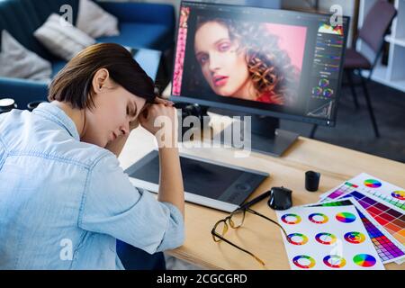 Portrait d'un graphiste fatigué travaillant des heures supplémentaires au bureau. Les travailleurs stressés présentent des symptômes de fatigue oculaire. Retoucher dans un studio photo. Épuisement Banque D'Images