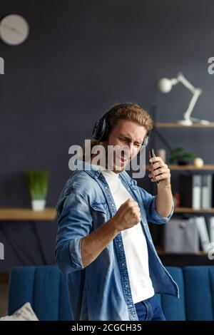 Beau homme aux cheveux longs avec des écouteurs qui écoutent de la musique, chantant et Dancing.drôle émotionnel souriant homme avec des écouteurs et téléphone mobile se détendre Banque D'Images