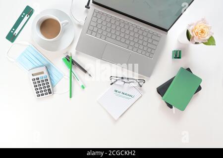 Bureau blanc avec ordinateur portable, services de travail écologiques, masque chirurgical contre le coronavirus et l'infection par le covid-19 et bloc-notes avec texte New Normal Banque D'Images