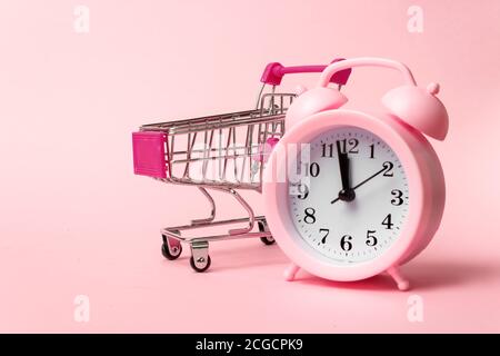 Gros plan du réveil et du panier sur fond rose. Vente, temps de réduction, concept de gain de temps. Vue de dessus, plan d'affichage avec espace de copie Banque D'Images