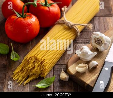 Pâtes à spaghetti crues attachées dans un paquet de tomates fraîches de vigne, d'ail et de basilic sur une table rustique en bois Banque D'Images