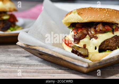 délicieux cheeseburger gastronomique avec des oignons rouges caramélisés, du fromage suisse, des cornichons et des tomates en filets Banque D'Images