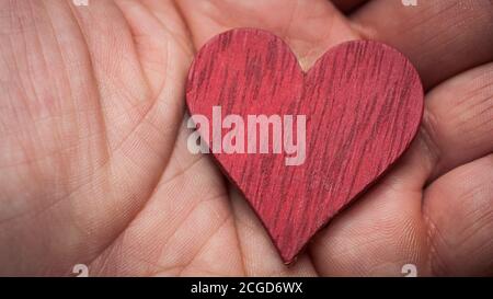 L'homme tient un coeur en bois rouge dans la paume de sa main Banque D'Images