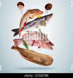 Poisson de mer frais avec des épices tombant, volant au-dessus de la planche de bois, isolé sur fond gris. Préparation des aliments, repas frais prêt pour la cuisson. Très haut Banque D'Images