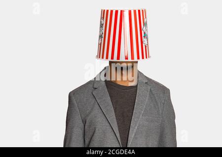 Anonyme ethnique mâle dans des vêtements élégants et décontractés portant du pop-corn à rayures godet sur tête sur fond gris Banque D'Images