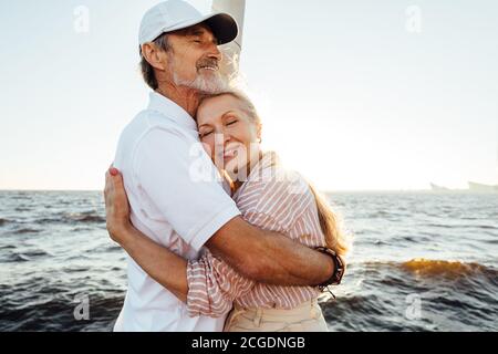 Couple senior affectueux qui s'embrasse sur un yacht privé. Belle femme mûre penchée sur la poitrine du mari avec les yeux fermés. Banque D'Images