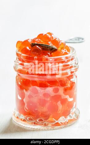 Caviar de saumon rouge dans un pot en verre sur fond blanc en bois, mise au point sélective Banque D'Images