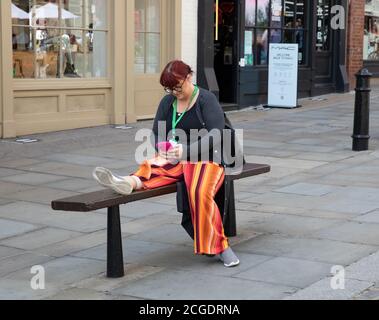 Une dame portant un tournesol Lanyard se repose sur un Banc à Londres tout en regardant son téléphone Banque D'Images