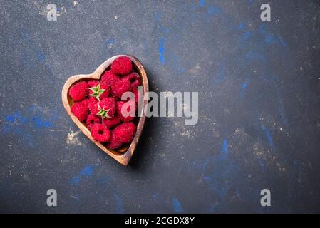 Framboises fraîches dans un bol en forme de coeur sur fond sombre, vue de dessus Banque D'Images