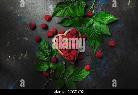 Framboises fraîches dans un bol en forme de coeur sur fond sombre, vue de dessus Banque D'Images