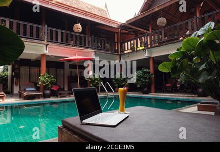 Un ordinateur portable blanc, un smartphone et un smoothie à la mangue sur un lit de soleil sur fond de piscine. Un début de journée. Concept d'entreprise freelance. Flexible RE Banque D'Images