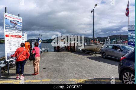 Les personnes inspectant l'horaire du ferry de l'île de Bere à Castletownbere, comté de Cork, irlande, alors que les véhicules partent du ferry. Banque D'Images