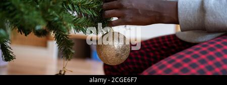 Image vue large une fille de couleur accrochant une boule de vacances dorée brillante sur l'arbre de noël. Banque D'Images