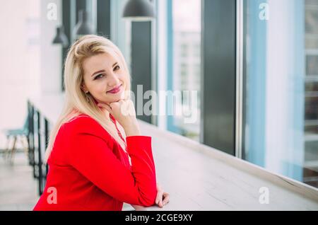 Belle femme d'affaires réussie dans un costume rouge dans un bâtiment de bureau léger près de la fenêtre Banque D'Images