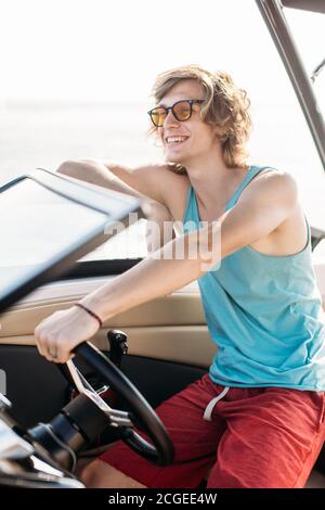 Un jeune homme blond dirige un bateau à moteur sur la mer pendant le coucher du soleil. Concept de voyage et de vacances en mer. Banque D'Images