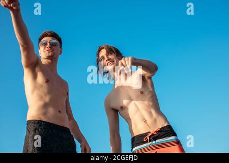Deux amis blancs heureux voyageant sur un yacht à la mer ouverte, bains de soleil sur l'arc du bateau pointant vers l'horizon. Loisirs et divertissement en mer. Banque D'Images