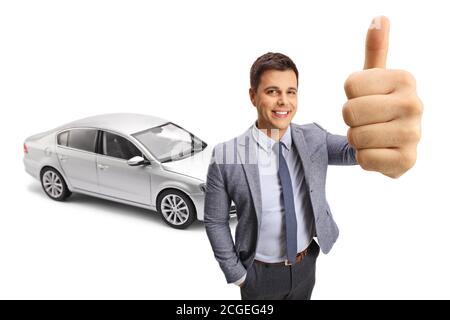 Un jeune homme heureux montrant un signe de pouce vers le haut devant d'une nouvelle voiture argentée isolée sur fond blanc Banque D'Images