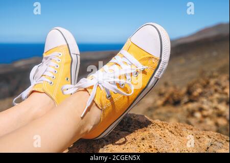 Vue rapprochée des pieds de femme portant des baskets . Voyageur assis sur Rock portant des baskets jaunes. Vacances d'été. Banque D'Images