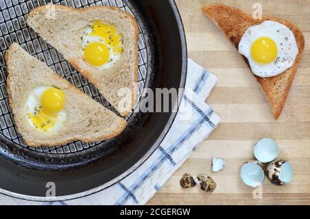 Tranches de pain frites avec œufs de caille sur une poêle placée sur une planche à découper en bois avec une serviette de cuisine et des coquilles d'œufs, vue de dessus. Une alimentation saine. Banque D'Images
