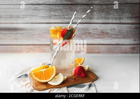 Limonade maison aux oranges, au citron, aux fraises et à la menthe dans un verre humide. Tasse avec gouttes d'eau et verseuse d'agrumes sur fond de bois. Si Banque D'Images