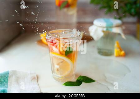 Limonade maison aux oranges, au citron, aux fraises et à la menthe dans un verre humide. Tasse avec gouttes d'eau et verseuse d'agrumes sur fond de bois. Si Banque D'Images