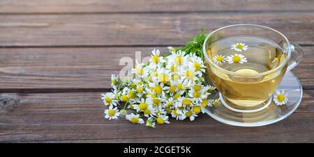 Thé camomille parfumé dans une tasse de verre et un bouquet de fleurs une table en bois avec un espace copie. Traitement à base de plantes. Banque D'Images