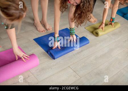 Vue rognée des mains des femmes déroulant des tapis de yoga colorés avant de pratiquer le yoga, en préparant pour l'exercice dans l'intérieur du studio Banque D'Images