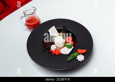 boules de crème glacée aux fraises et au sirop, décorées de feuilles de menthe dans un bol noir sur fond blanc Banque D'Images