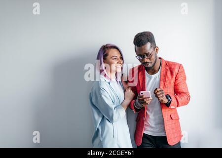 Amis multiraciale partage de photos avec les autres, isolés sur fond de mur gris, copiez l'espace. Banque D'Images