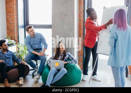 Des jeunes de différentes races et nationalités ayant l'esprit d'équipe, formation à la recherche à l'African man présentant ses idées sur le tableau de fl Banque D'Images