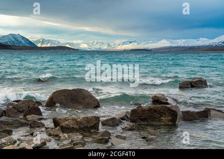 Vue panoramique sur les montagnes et le lac Tekapo le jour où les fortes vagues frappent les rochers au bord de l'eau à Canterbury, Nouvelle-Zélande. Banque D'Images