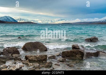 Vue panoramique sur les montagnes et le lac Tekapo le jour où les fortes vagues frappent les rochers au bord de l'eau à Canterbury, Nouvelle-Zélande. Banque D'Images