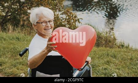 femme âgée en fauteuil roulant près de la rivière tenant une montgolfière en forme de cœur. Photo de haute qualité Banque D'Images